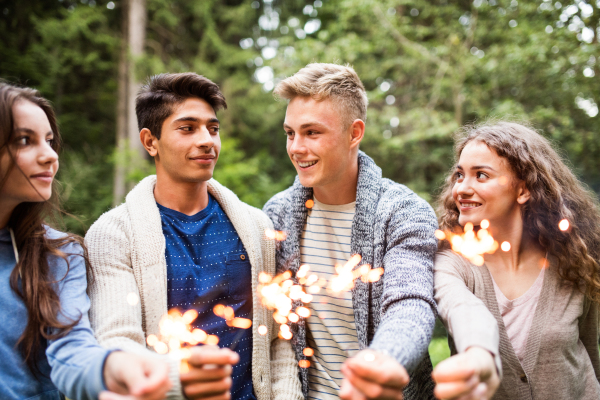 Group of teenagers in forest at bonfire with sparklers.