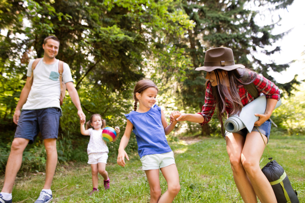 Beautiful young family with cute little daughters going camping in forest.