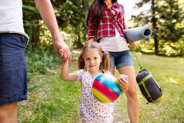 Unrecognizable parents with cute little daughter camping in forest.