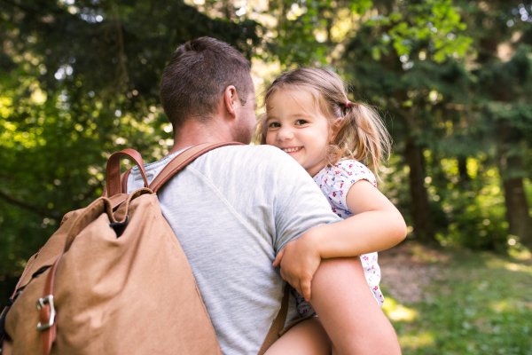 Unrecognizable young father with backpack carrying his cute little daughter going to camp in forest.