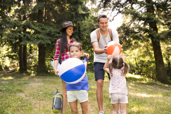 Beautiful young family with cute little daughters going camping in forest.