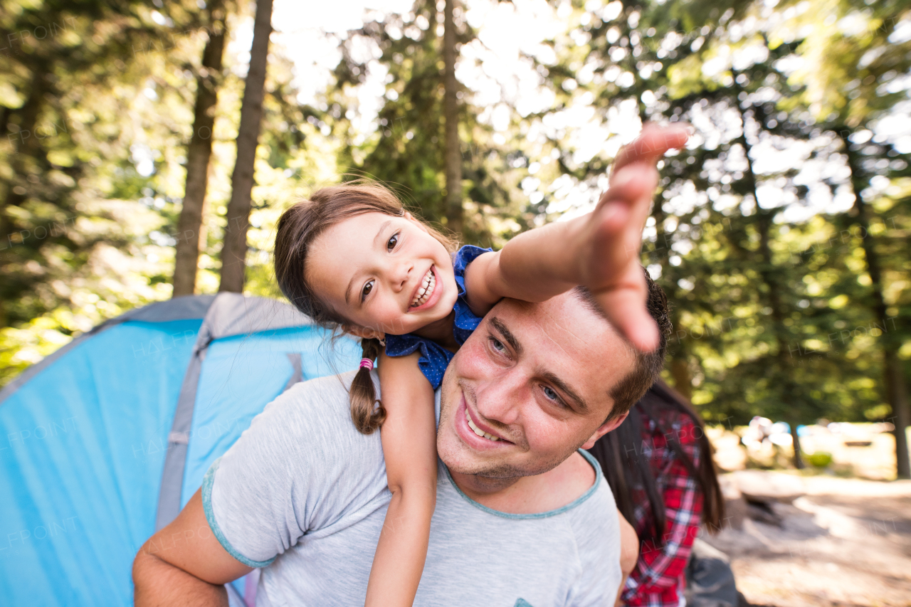 Handsome young father with cute little daughter camping in forest, sitting in front of tent.