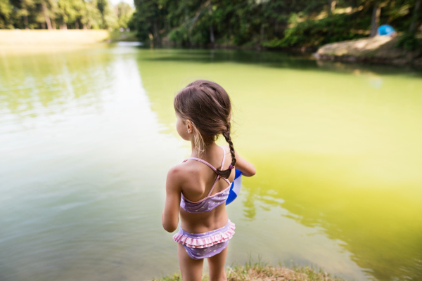 Cute little girl in swimming suit standing at the the lake. Summer heat and water.