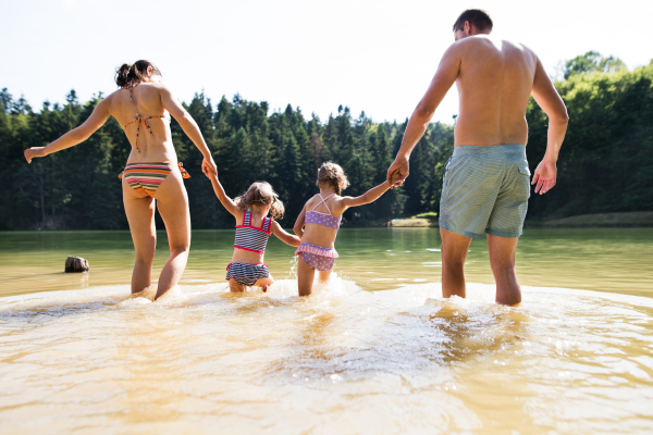 Young mother and father with their little daughters in the the lake. Summer heat and water. Rear view.