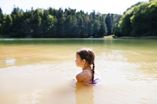 Cute little girl in swimming suit standing at the the lake. Summer heat and water.