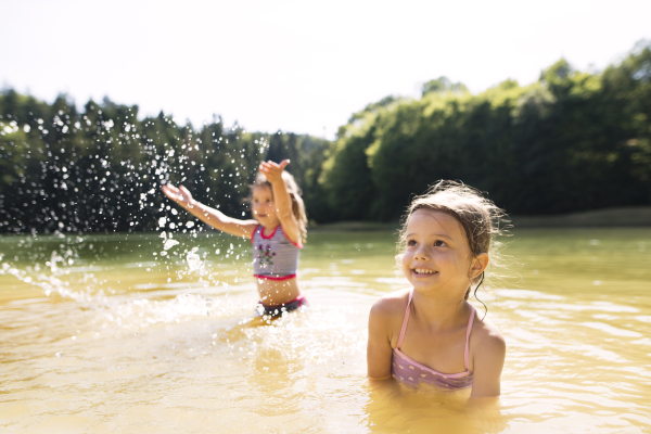 Cute little girls in swimming suit standing in the lake. Sisters playing in water. Summer heat and water.