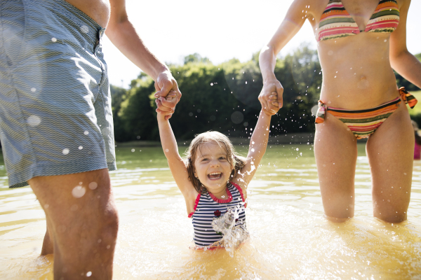 Unrecognizable mother and father with their daughter in the the lake. Summer heat and water.