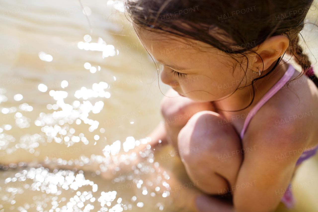 Cute little girl in swimming suit playing in the the lake. Summer heat and water.