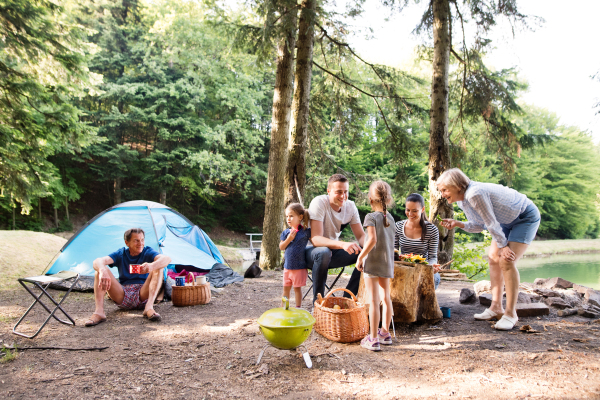 Beautiful family enjoying camping holiday in forest. Barbecue with drinks and food.