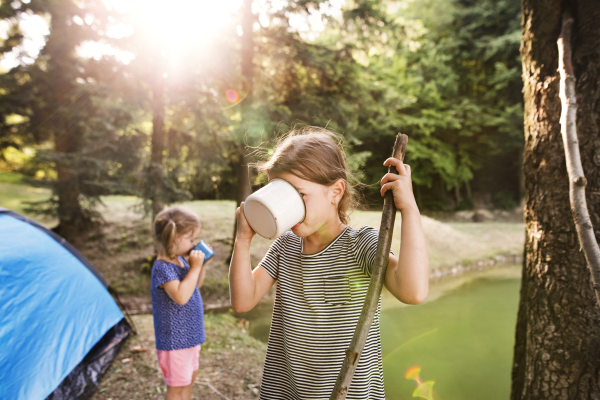 Cute little girls camping outdoors, drinking water from a big enameled mug.