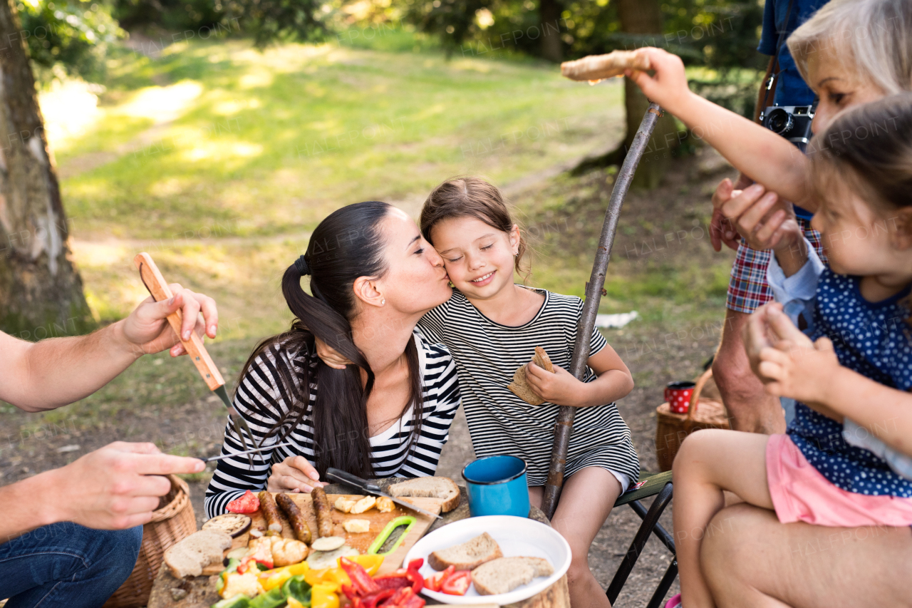 Beautiful family enjoying camping holiday in forest, eating together. Barbecue with drinks and food.