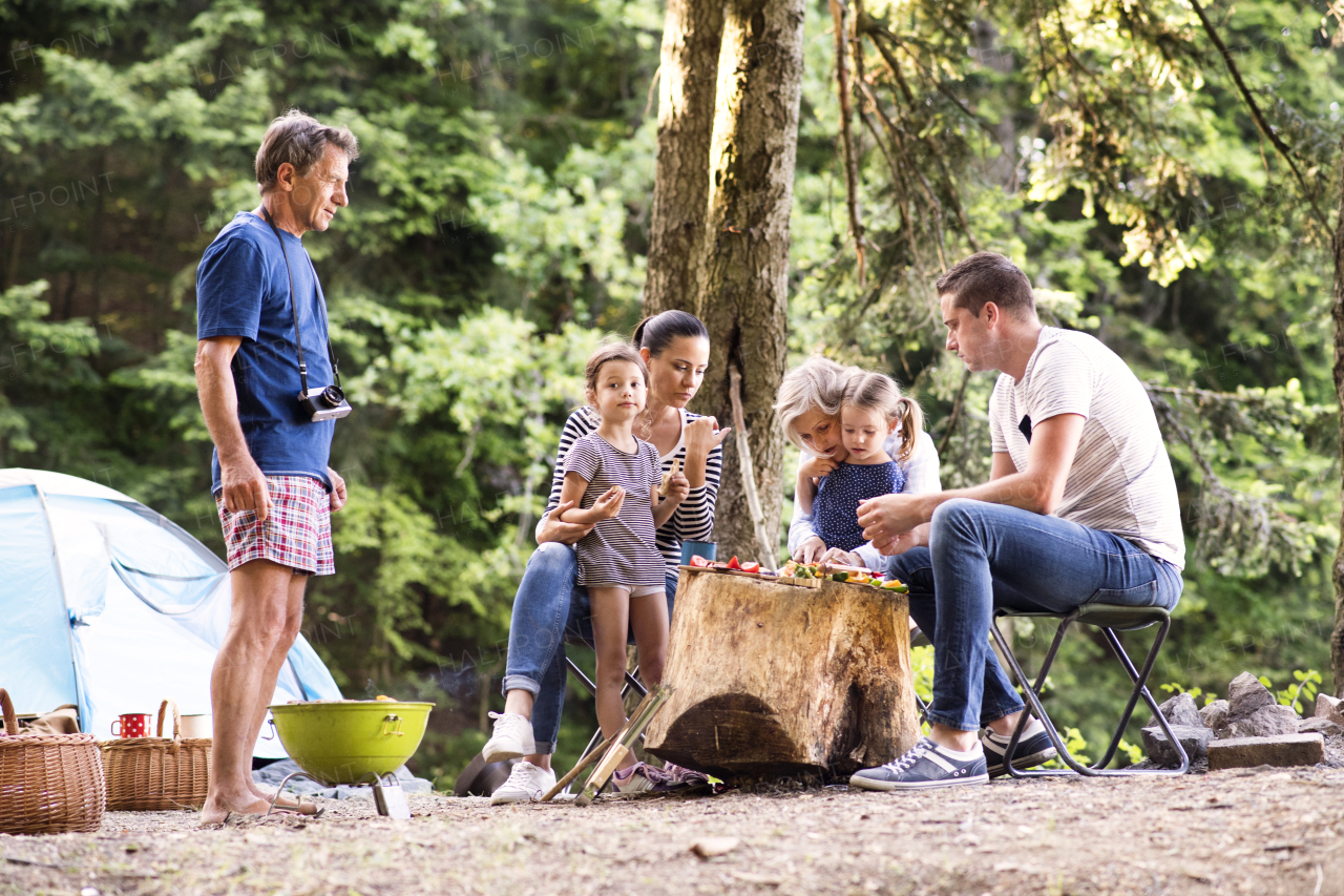 Beautiful family enjoying camping holiday in forest. Barbecue with drinks and food.