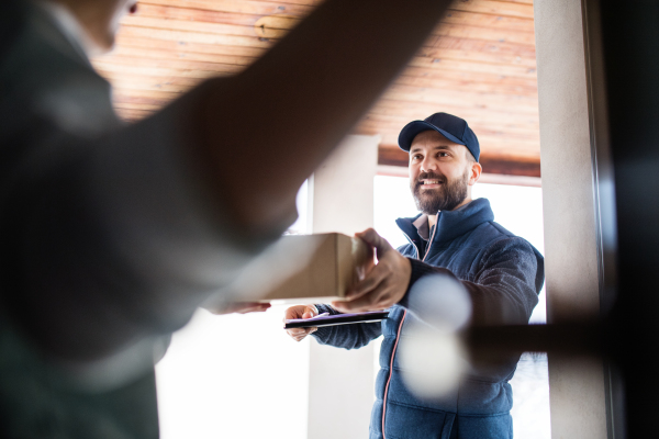 Unrecognizable woman receiving parcel from delivery man at the door - courier service concept.