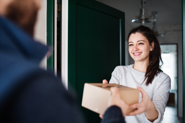 Woman receiving parcel from unrecognizable delivery man at the door - courier service concept.