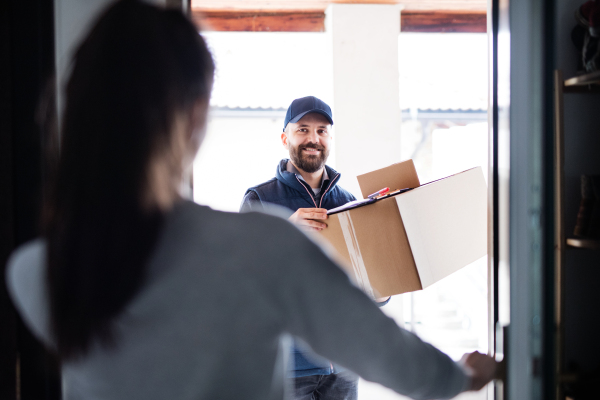 Unrecognizable woman receiving parcel from delivery man at the door - courier service concept.