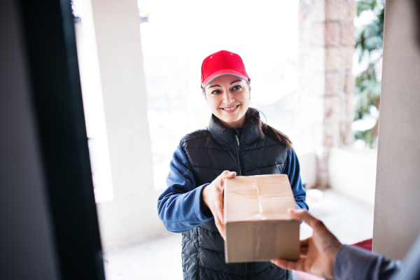 An unrecognizable man receiving parcel from delivery woman at the door - courier service concept.