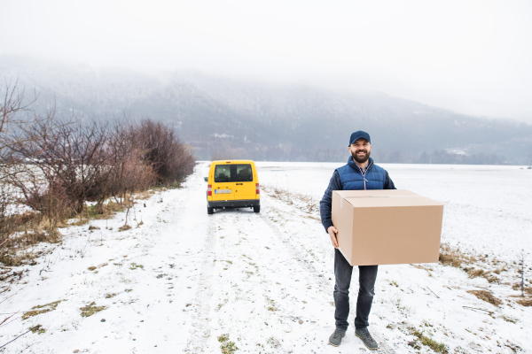 Delivery man delivering parcel box to recipient - courier service concept. A man with a smartphone making a phone call.