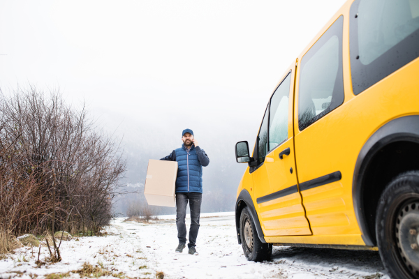 Delivery man delivering parcel box to recipient - courier service concept. A man with a smartphone making a phone call.