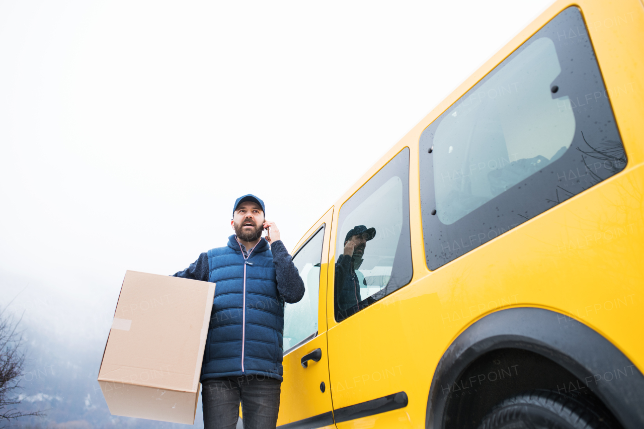 Delivery man delivering parcel box to recipient - courier service concept. A man with a smartphone making a phone call.