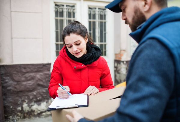 Young woman receiving parcel from delivery man at the door - courier service concept.