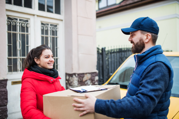 Young woman receiving parcel from delivery man at the door - courier service concept.