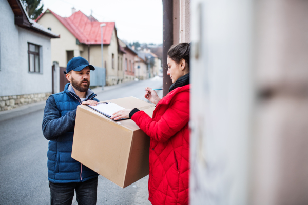 Young woman receiving parcel from delivery man at the door - courier service concept.