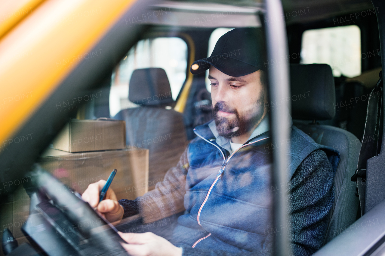 Delivery man delivering parcel box to recipient - courier service concept. A man signing a document. Shot through glass.