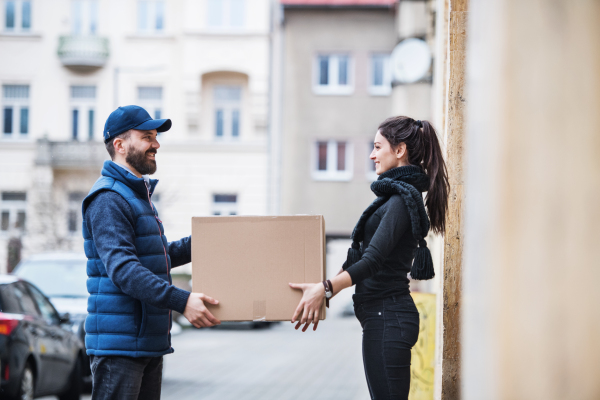 Young woman receiving parcel from delivery man at the door - courier service concept.