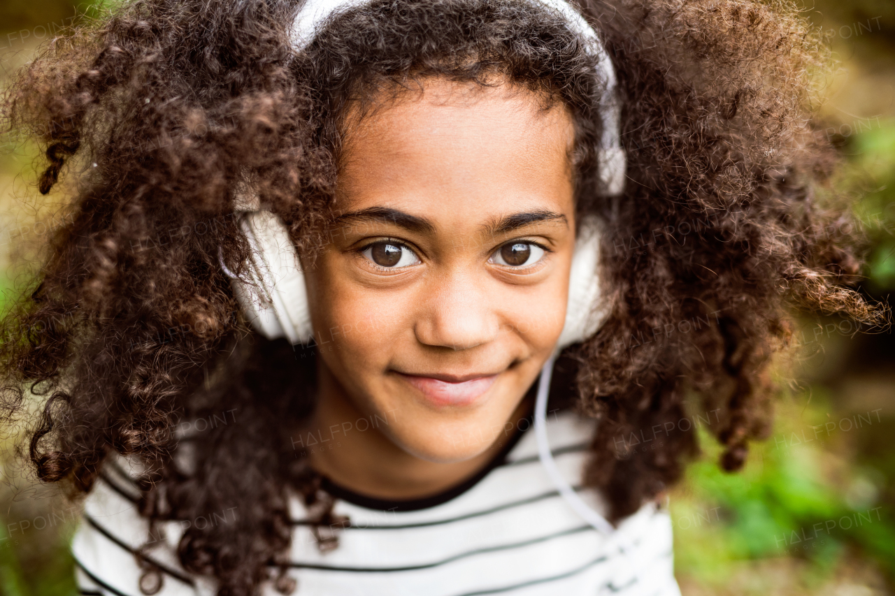 Beautiful african american girl with curly hair outdoors, wearing headphones, listening music.