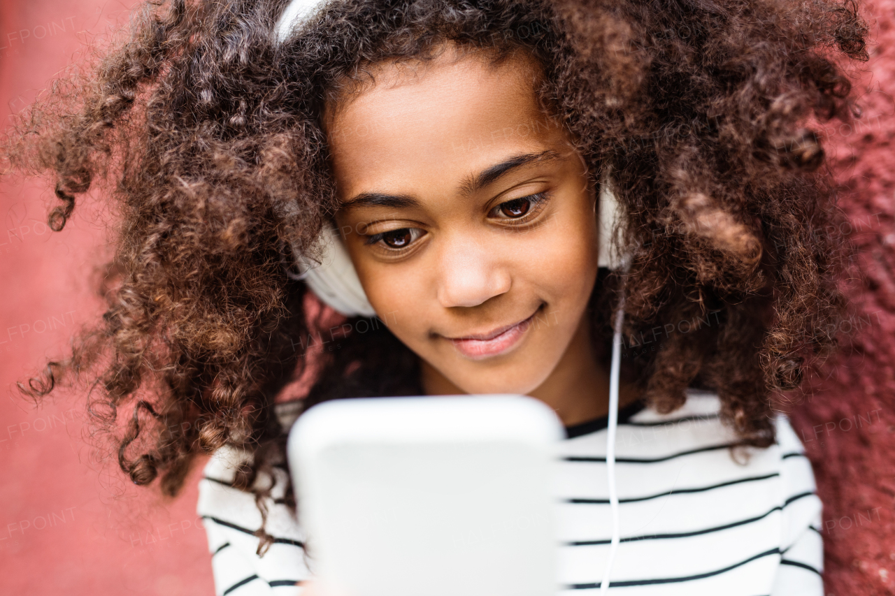 Beautiful african american girl with curly hair, holding smart phone, wearing headphones, listening music.