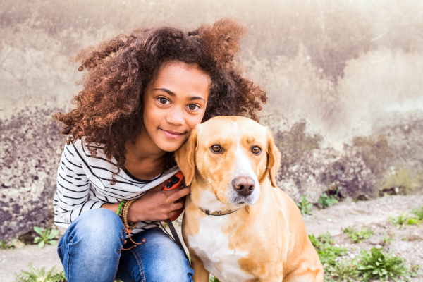 Beautiful african american girl with curly hair outdoors with her cute dog against old concrete wall.