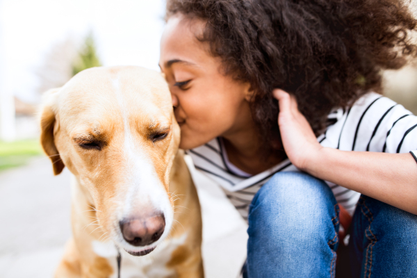 Beautiful african american girl with curly hair outdoors with her cute dog, kissing him.