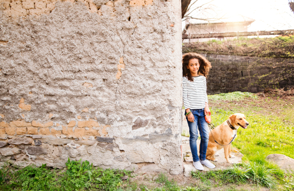 Beautiful african american girl with curly hair outdoors with her cute dog at the old concrete wall.