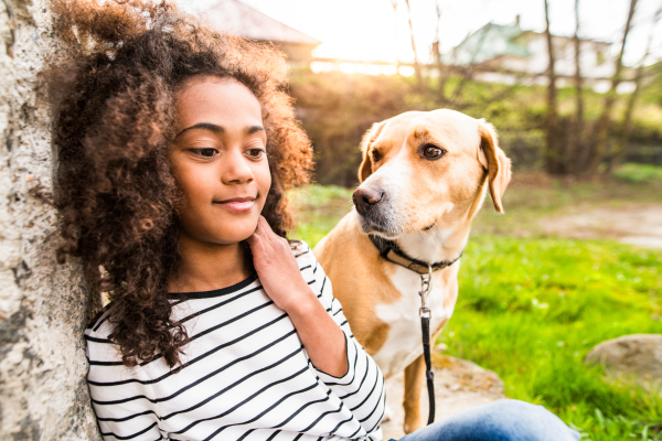 Beautiful african american girl with curly hair outdoors with her cute dog at the old concrete wall.