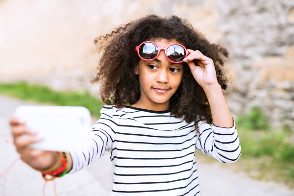 Beautiful african american girl with curly hair, holding smart phone, taking selfie.