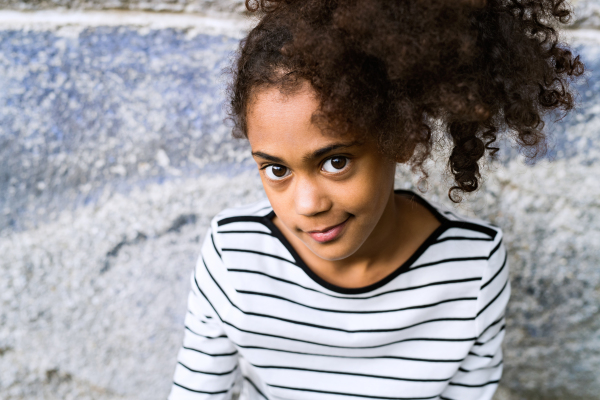 Beautiful african american girl with curly hair outdoors wearing striped t-shirt against old concrete wall.