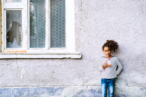 Beautiful african american girl with curly hair outdoors drinking juice from glass. Old house background.