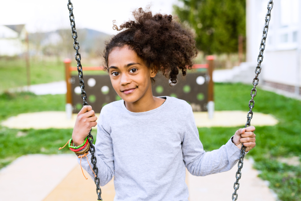 Beautiful african american girl with curly hair outdoors wearing gray sweatshirt, sitting on swing.