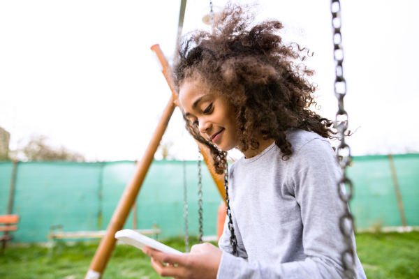 Beautiful african american girl on swing with smart phone writing text message or reading something.