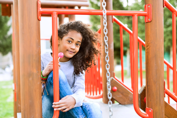 Beautiful african american girl on playground eating lollipop.