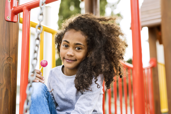 Beautiful african american girl on playground eating lollipop.