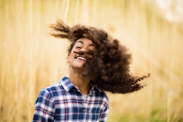 Beautiful african american girl with curly hair in checked shirt outdoors in field.