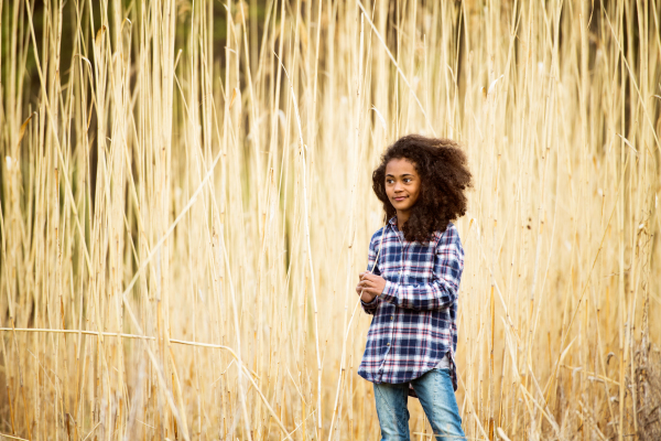 Beautiful african american girl with curly hair in checked shirt outdoors in field.