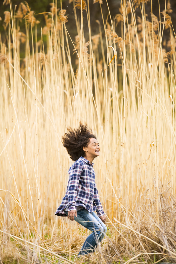 Beautiful african american girl with curly hair in checked shirt outdoors in field jumping.