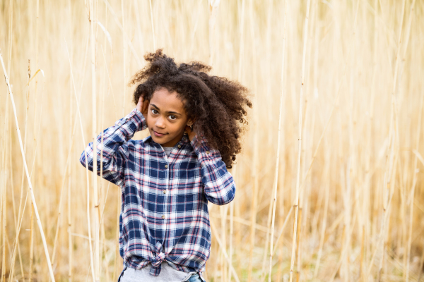 Beautiful african american girl with curly hair in checked shirt outdoors in field.