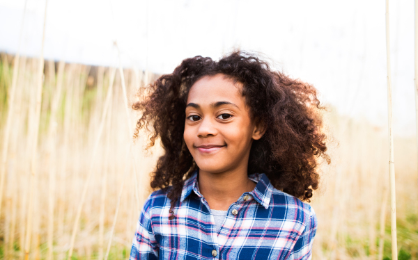 Beautiful african american girl with curly hair in checked shirt outdoors in field.