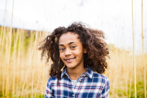 Beautiful african american girl with curly hair in checked shirt outdoors in field.