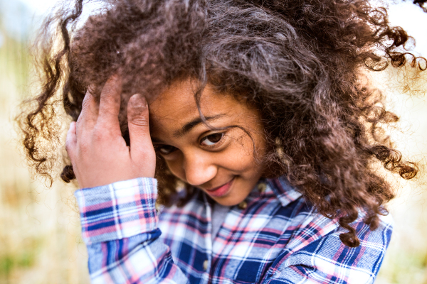 Beautiful african american girl with curly hair in checked shirt outdoors in field.