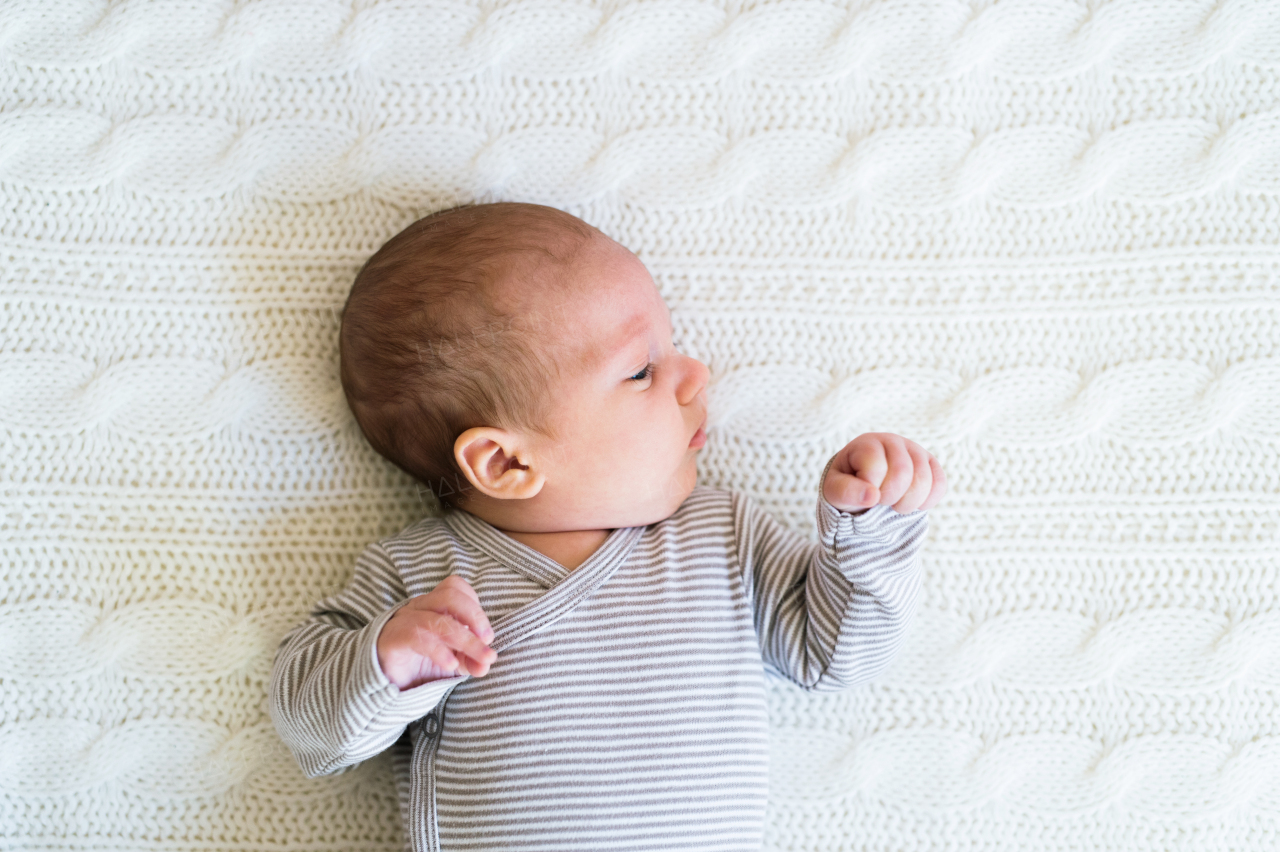 Cute newborn baby boy in striped onesie lying on bed, close up