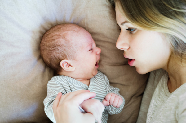 Beautiful young mother with her cute baby son lying on bed in bedroom